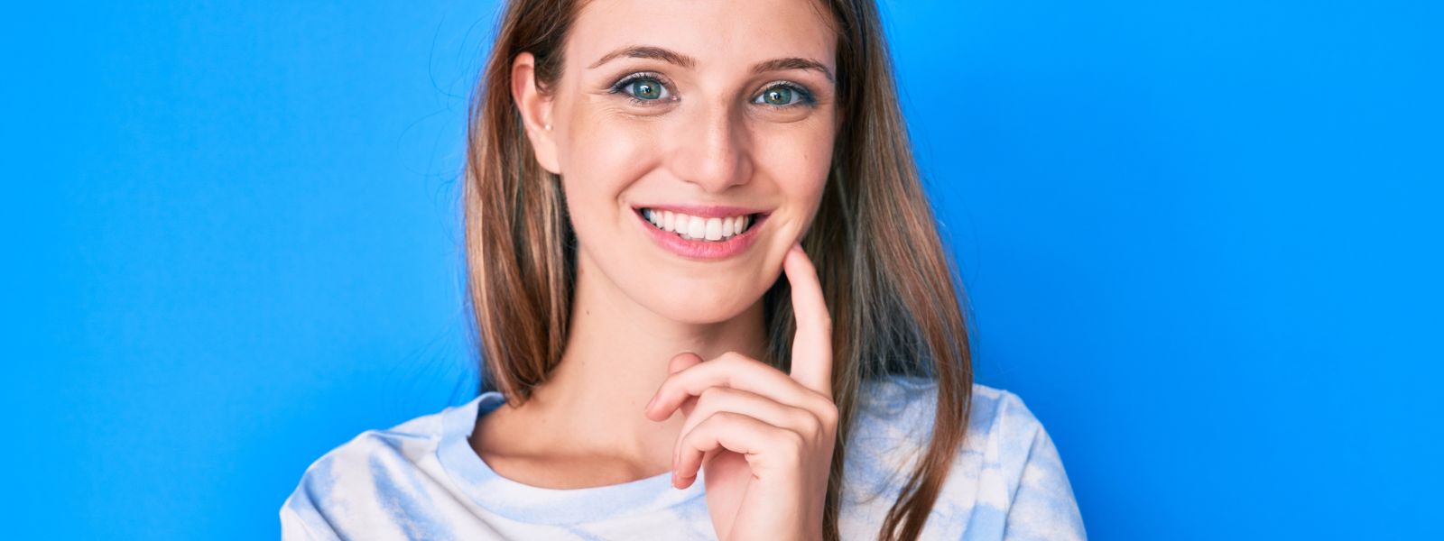 Girl in a blue background with a finger on a cheek.